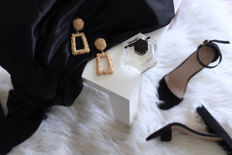 Luxury Goods - pair of gold-colored earrings on table and black ankle-strap pumps on area rug